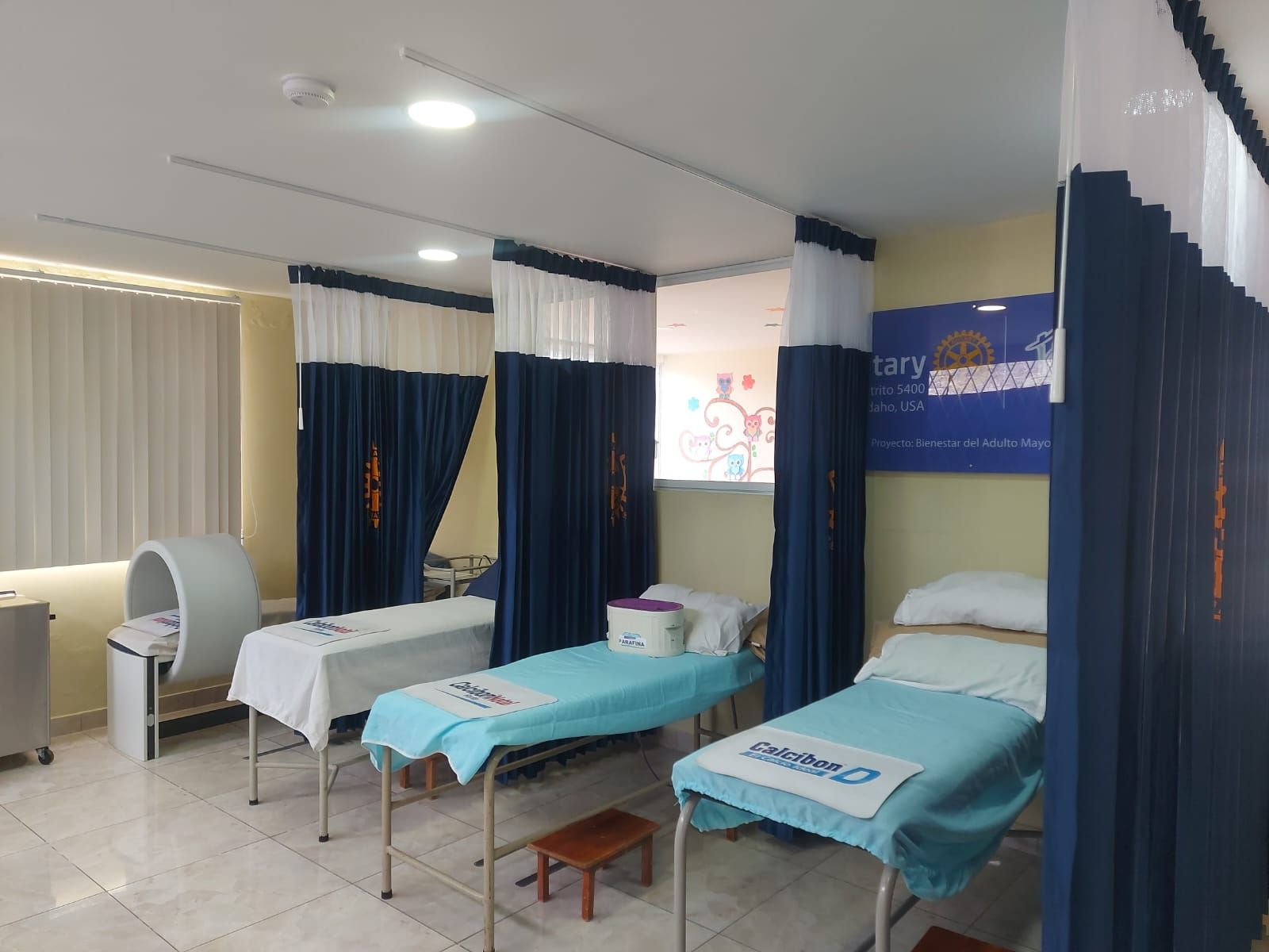 Vista general de la sala de fisioterapia con camillas, cortinas de privacidad y equipo de magnetoterapia